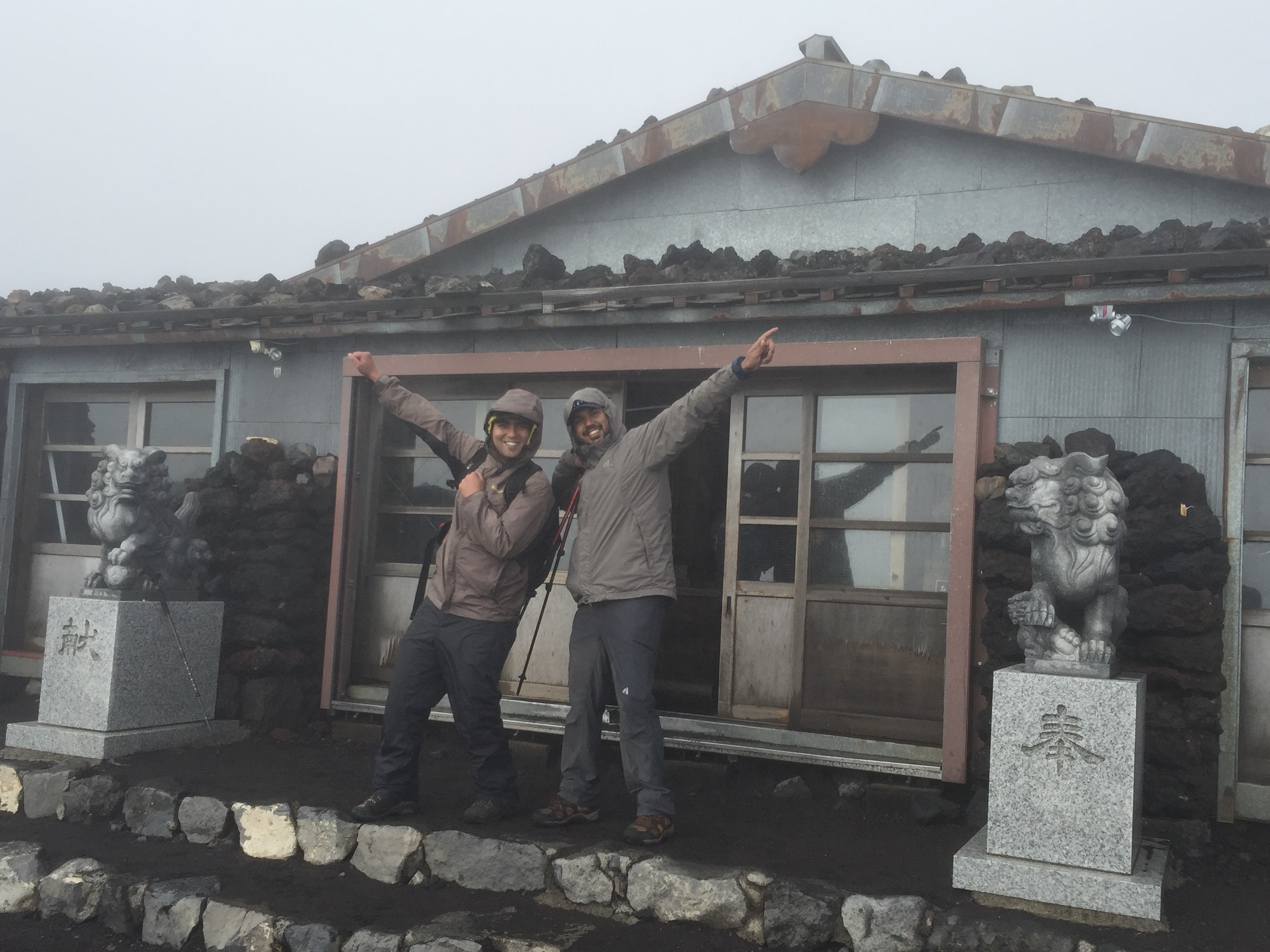 At a quiet shrine near the summit of Mount Fuji, Japan — my friend and I standing beside offerings to Konohanasakuya-hime, the goddess of volcanoes and blossoms.